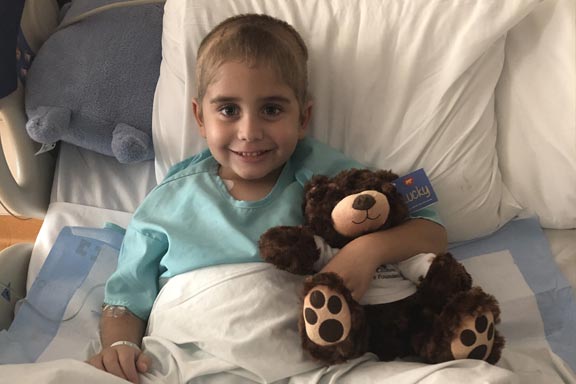 child in hospital bed with golden teddy bear